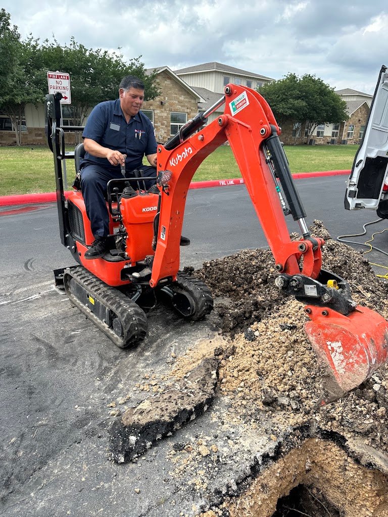 San Antonio Plumbing technician operating a mini excavator to repair a broken sewer line in a parking lot.